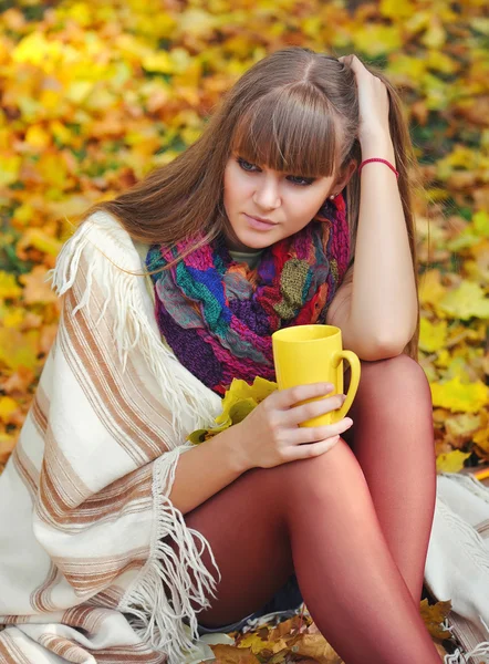 Joven mujer hermosa que sostiene la taza de té en las manos sobre un fondo hojas de otoño — Foto de Stock