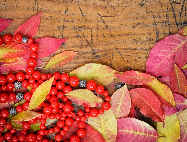 Sonbahar yaprakları ve ahşap arka plan üzerinde kırmızı boncuklar — Stok fotoğraf