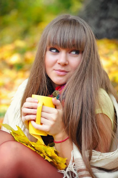 Sonbahar yaprakları fincan çay bir arka plan üzerinde elinde tutan genç güzel kadın — Stok fotoğraf