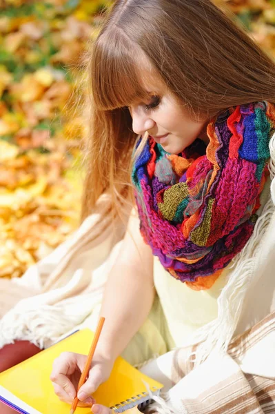 Mooi meisje met notitieblok op een achtergrond herfst bladeren — Stockfoto