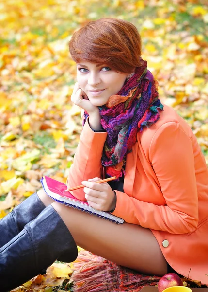 Рыжая студентка с блокнотом на заднем плане осенние листья — стоковое фото