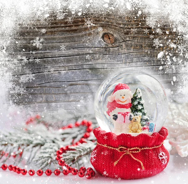 Um globo de neve com boneco de neve no fundo de madeira coberto de neve — Fotografia de Stock