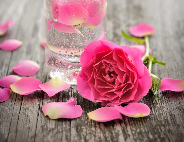 Olio essenziale con petali di rosa su fondo di legno — Foto Stock