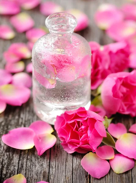 Óleo essencial com pétalas de rosa sobre fundo de madeira — Fotografia de Stock