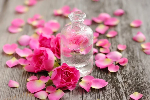 Olio essenziale con petali di rosa su fondo di legno — Foto Stock