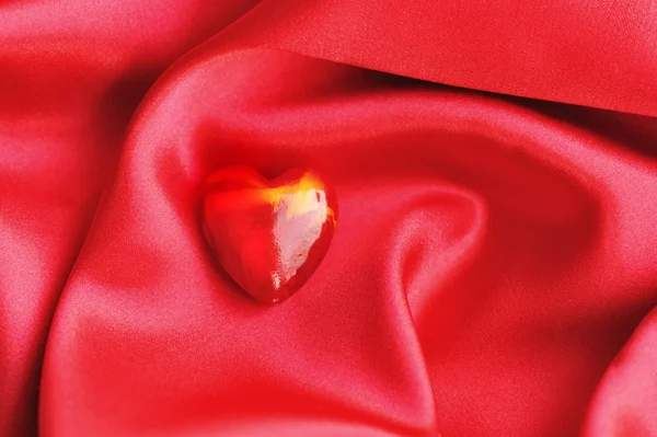 Corazón rojo sobre fondo de tela satinada — Foto de Stock