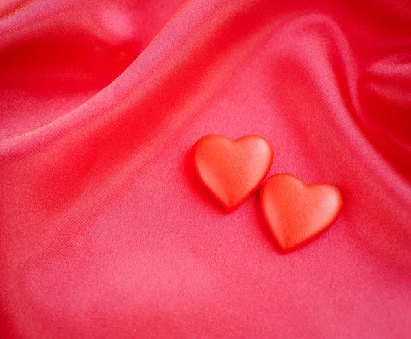Two red hearts on satin fabric background — Stock Photo, Image