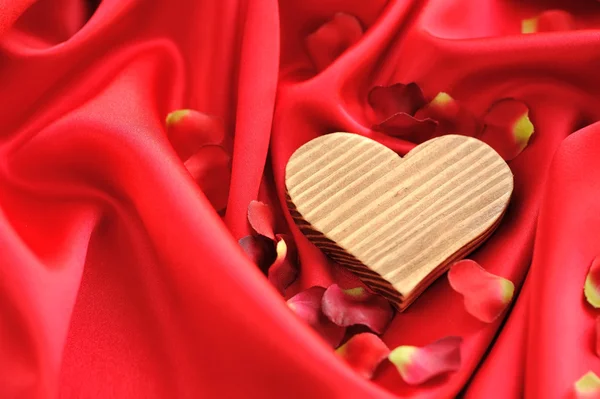 Wooden Heart on a background of red petals and satin — Stock Photo, Image