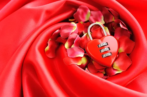 Lucchetto a forma di cuore su uno sfondo di petali rossi e raso — Foto Stock