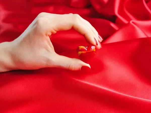 Декоративное сердце в женской руке на фоне красного шелка — стоковое фото