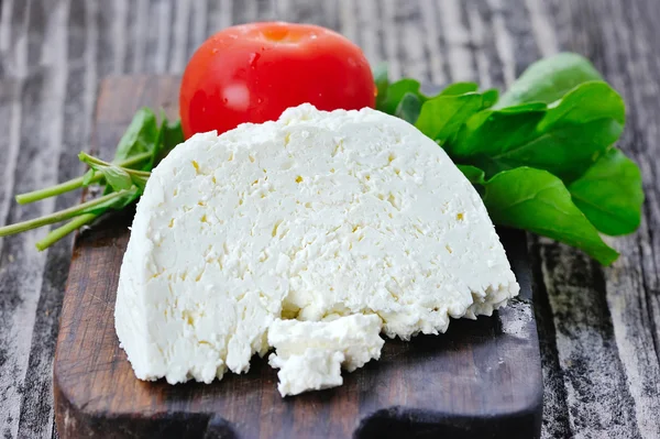 Queijo com tomates e cebola em uma tábua de madeira — Fotografia de Stock