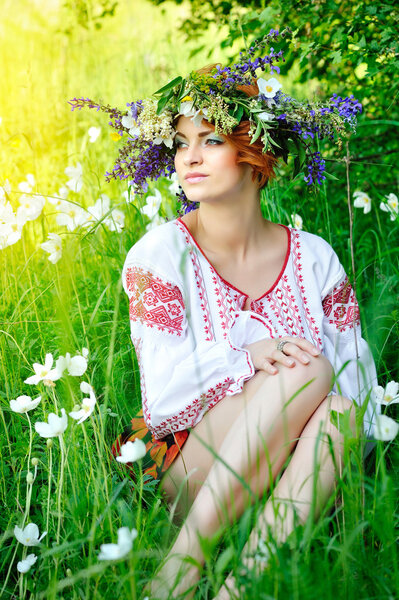 Young beautiful woman in the Ukrainian national costume in flowering meadow