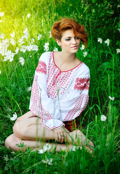 Young beautiful woman in the Ukrainian national costume in flowering meadow — Stock Photo, Image