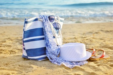 şapka, çanta, güneş gözlüğü ve kumlu bir plaj üzerinde flip flop. VA yaz