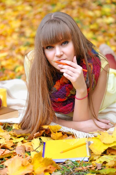 Schöne Mädchen mit Notizbuch auf einem Hintergrund Herbstblätter — Stockfoto