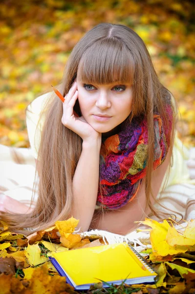 Mooi meisje met notitieblok op een achtergrond herfst bladeren — Stockfoto