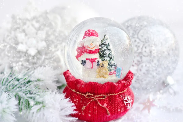 Um globo de neve com boneco de neve no fundo ramos de abeto com neve — Fotografia de Stock