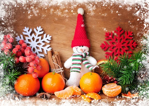 Snowman with tangerines and branches of fir and Christmas decorations on a wooden background — Stock Photo, Image