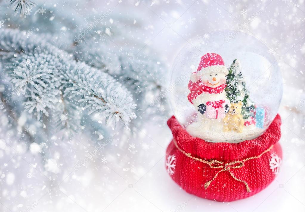 A snow globe with snowman on a background snow-covered fir branches