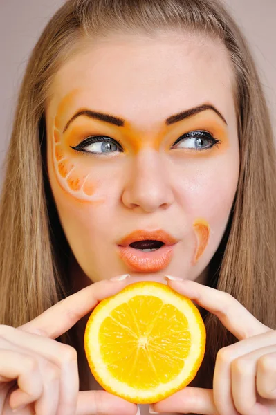 Jonge mooie vrouw met creatieve oranje make-up met oranje in haar hand — Stockfoto