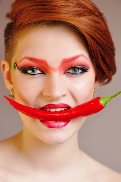 Portret van mooie vrouw met creatieve rode make-up bijten chili peper — Stockfoto