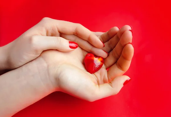 Decoratieve hart in handen van de vrouw tegen een achtergrond van rode zijde — Stockfoto