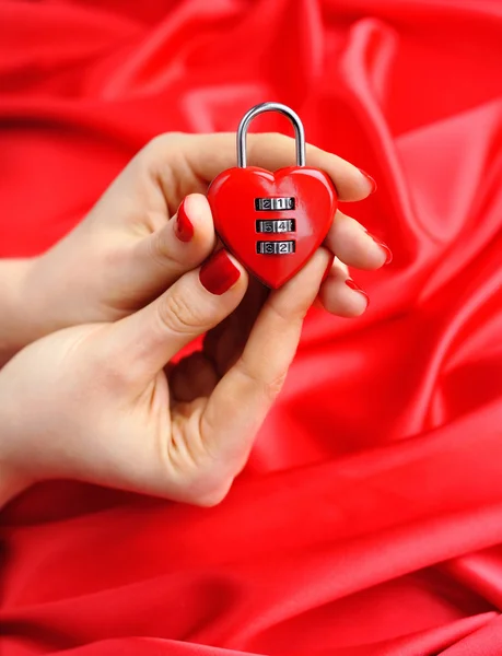 Lucchetto a forma di cuore nelle mani delle donne su uno sfondo di seta rossa — Foto Stock