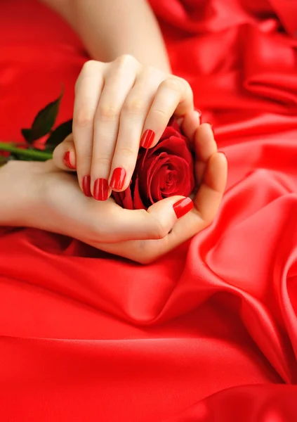 Rose rouge dans les mains des femmes sur un fond de soie rouge — Photo