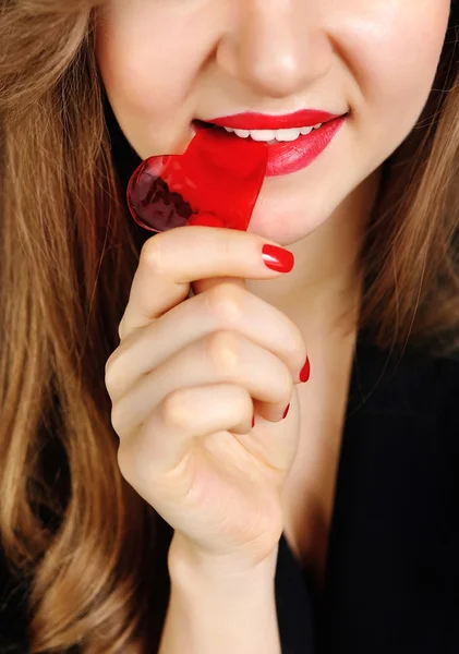 Beautiful girl biting red heart candy — Stock Photo, Image