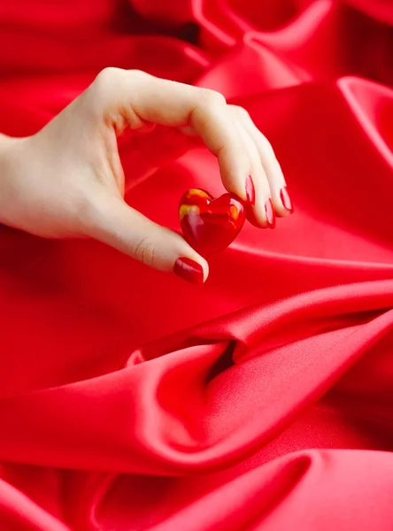 Decorative Heart in women's hands against a background of red silk — Stock Photo, Image