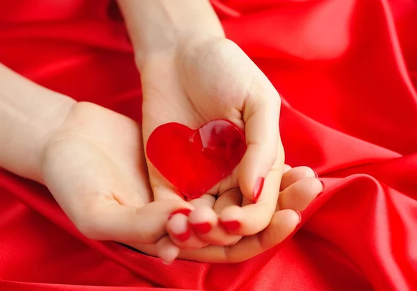 Heart candy in women's hands against a background of red silk — Stock Photo, Image