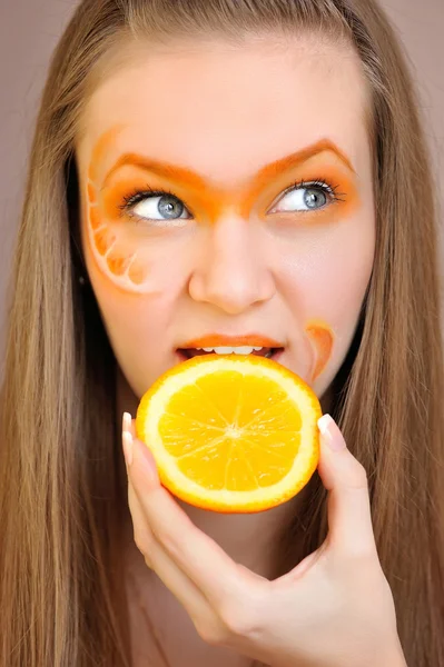 Jonge mooie vrouw met creatieve oranje make-up eten een oranje — Stockfoto