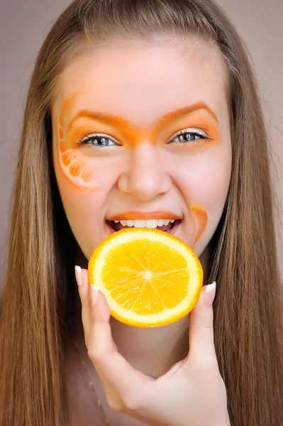 Jonge mooie vrouw met creatieve oranje make-up eten een oranje — Stockfoto