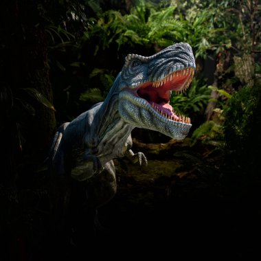 Ormandaki kızgın bir T-Rex dinozor heykelinin yakın görüntüsü. Ağzı açık ve keskin dişleri olan korkunç bir hayvan.