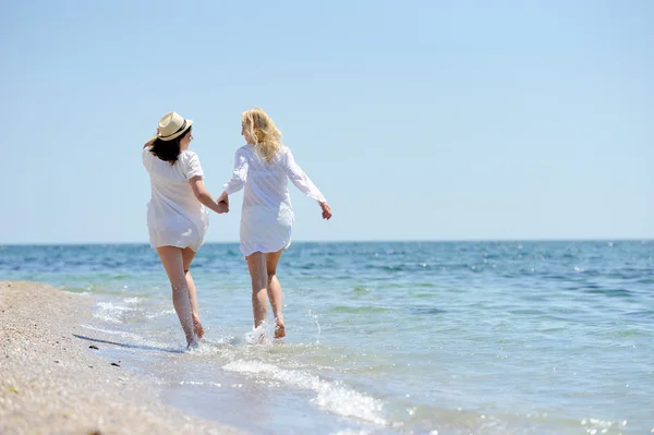 A fehér ruha a tengerparton fut két womans — Stock Fotó