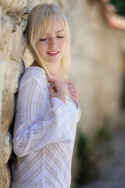 Schöne blonde Frau steht an einer Steinmauer — Stockfoto