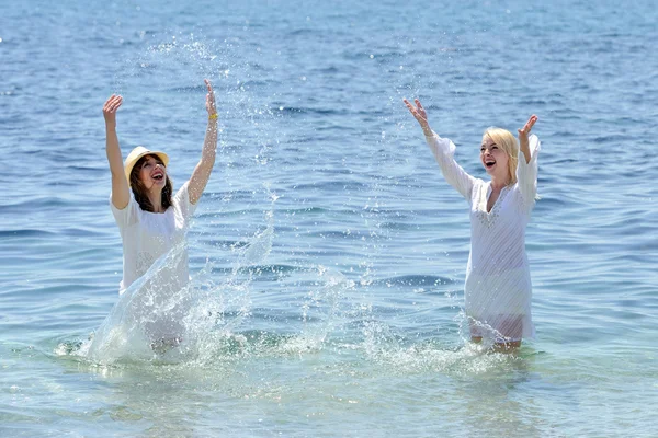 Two young smiling womans splashing water in sea — Stock Photo, Image