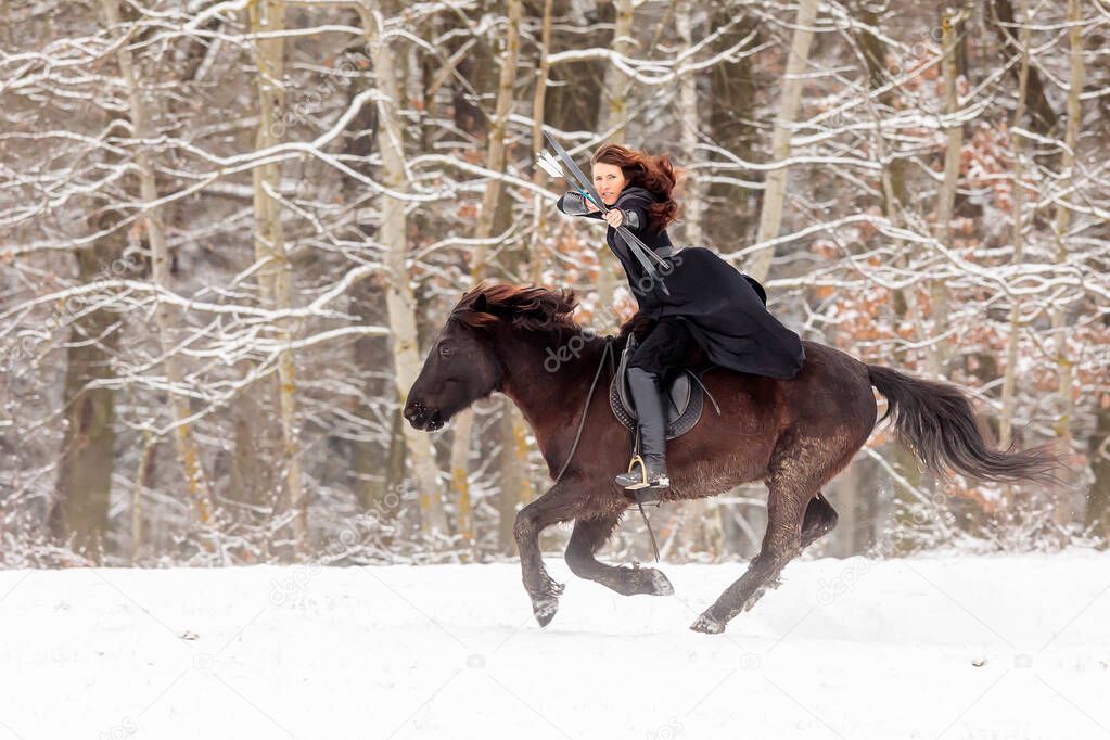 woman riding in historical costume as a warrior quickly gallops through the snowy landscape and shot from the bow