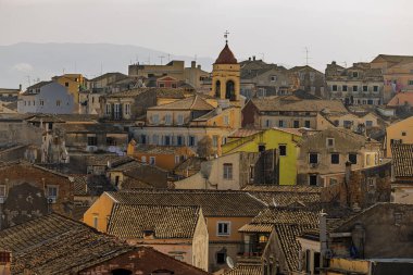 The historic center of Corfu Town (Kerkyra) shows its pastel-colored houses and red church tower glowing in warm evening light.