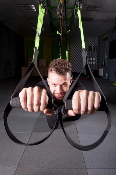 Bonito jovem musculoso homem formação com trx enquanto exercitando no ginásio — Fotografia de Stock