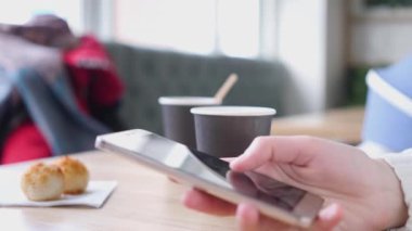 Bir fincan kahvenin arka planında ellerinizi birleştirin. Kız akıllı telefonuyla mesajlaşıyordu. Masanın üzerinde bir fincan kahve var. Bir kafede oturuyor.