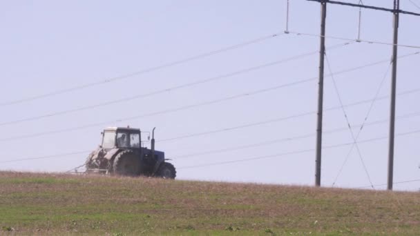 トラクターは、火力発電所のパイプを背景にフィールドを通って駆動します。作付トラクターは作物を植えるための農地を準備します. — ストック動画