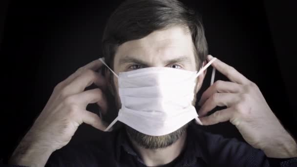 Retrato de um homem colocando uma máscara médica em um fundo preto, tiro de estúdio. O conceito de prevenção de doenças virais e outras — Vídeo de Stock
