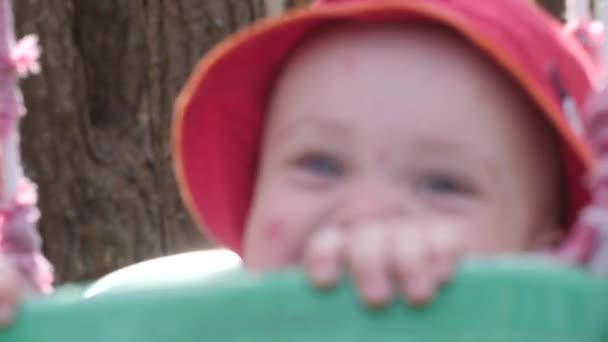 Šťastné dítě v červené panamě se houpe na houpačce. Ten kluk se směje. Léto. Šťastné dětství — Stock video