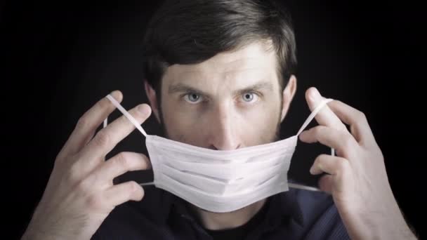 Fehér férfi a szobában fekete háttérrel orvosi maszkot visel. Légszennyezés, szmog. Légzőszervi betegségek elleni védelem. Pandémia. Járvány. Új kép az emberi életről — Stock videók