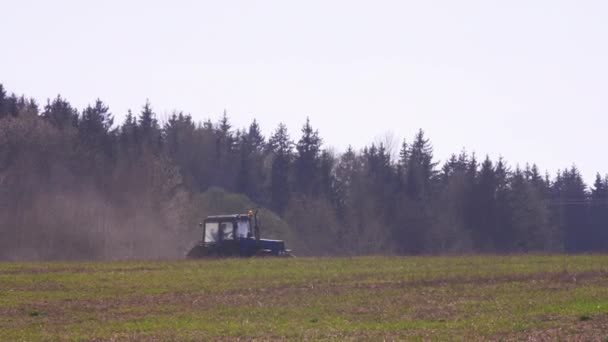 Trator azul com um arado reverso arado um campo contra o fundo de uma bela floresta verde. Trabalho agrícola no domínio do agronegócio — Vídeo de Stock