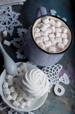 Gri arka planda marshmelow olan bir fincan Noel kakaosu. Bir fincan yeni yıl ve noel kakaosu içinde marshmallowlar, örgü beyaz kar taneleri, şekerler ve Noel süslemeleri.