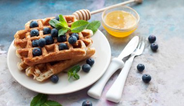 Beyaz tabakta yaban mersinli Belçika waffle 'ı, bal ve nane şekeri. Tatlı waffle 'lı kahvaltı. Beyaz saplı çatal ve bıçak.