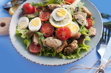 Mavi arka planda midye, domates, yumurta, roka, ıspanak, limon ve kızarmış ekmek salatası. Üzüm soslu deniz ürünleri salatası.