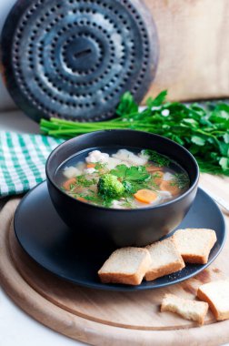 Brokolili sebze çorbası, karnabahar, havuç, patates, maydanoz ve dereotlu siyah kase.